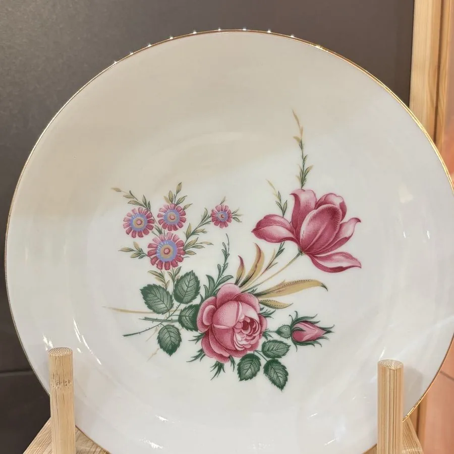 Assiette ancienne à décor floral rose et vert, dressée sur un socle de bois.