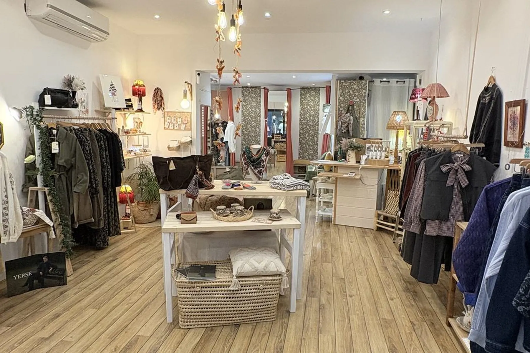 Vue en enfilade de la boutique : parquet clair, portants de part et d’autre, table centrale et fond éclairé.