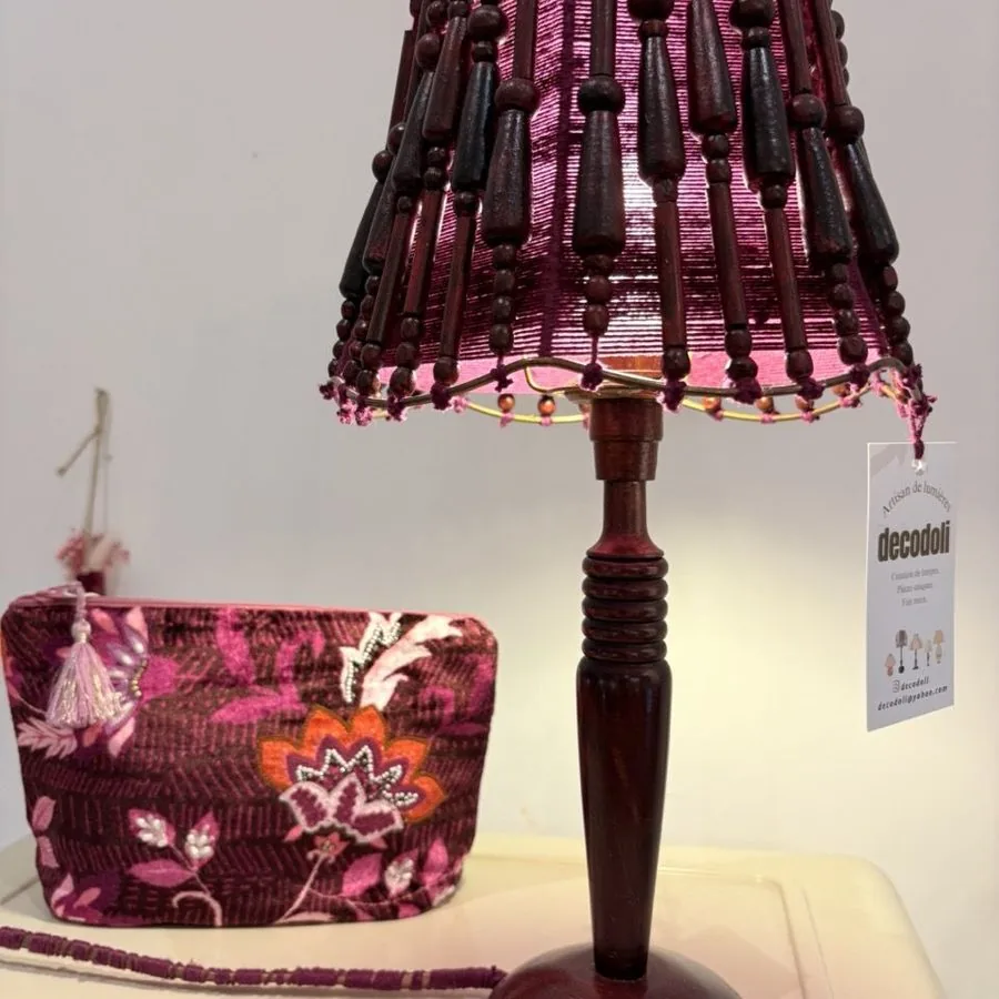 Grande lampe à abat-jour frangé orange, au milieu de vases peints et de verrerie.
