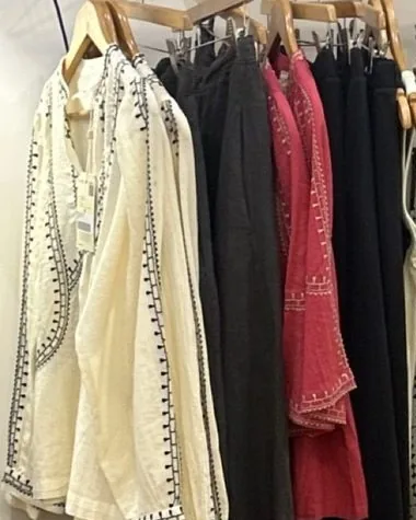 Pièces Indi&Cold sur un portant de bois, blouse écrue brodée, chemise rouge et robes aux imprimés.
