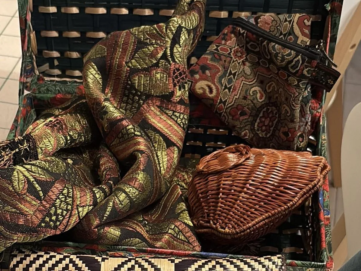 Malle ouverte débordant de textiles imprimés aux motifs paisley et d’un panier tressé.