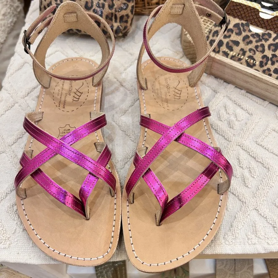Sandales spartiates à lanières croisées rose métallisé, sur un plaid clair.