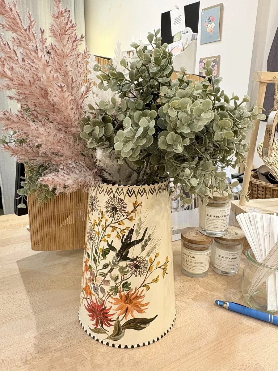 Un vase de céramique peinte à la main, garni de fleurs séchées, entouré de petits objets chinés.