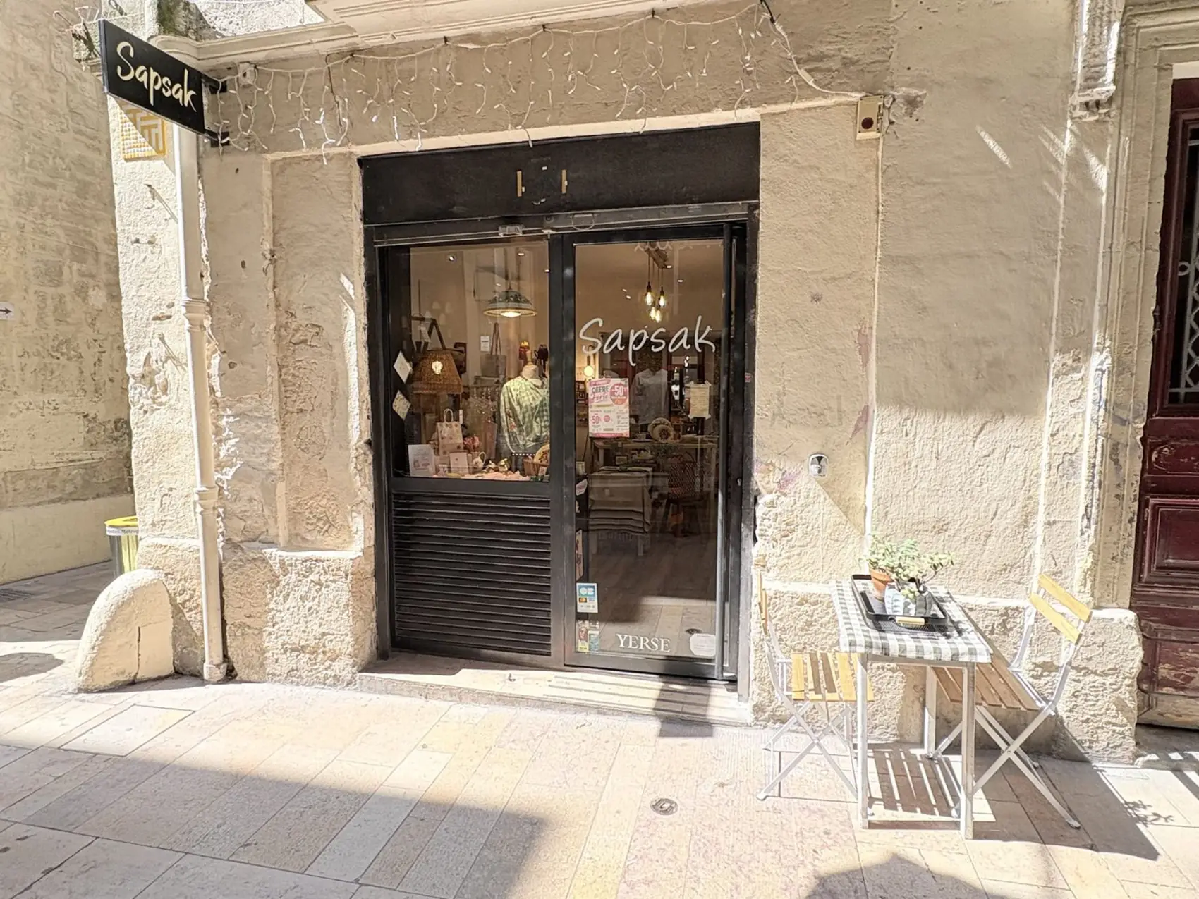 La vitrine de Sapsak vue de la rue, encadrée de volets de bois noir, éclairée de l’intérieur.