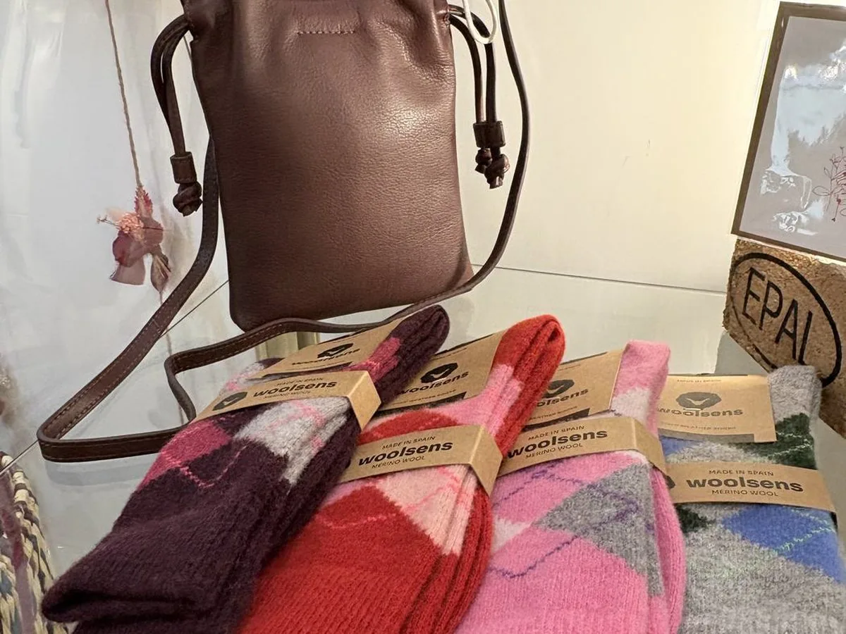 Chaussettes de laine mérinos aux teintes prune, rose et grise, et une pochette de cuir, posées côte à côte.