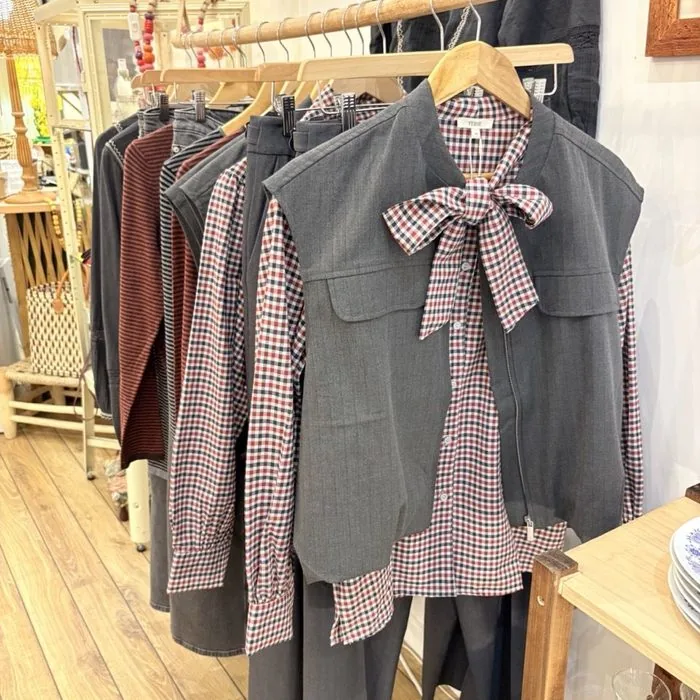 Gilet gris à nœud et chemise vichy Yerse, sur un portant de bois.
